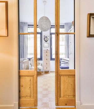 Interior of white room with baby crib and armchair near window with blue chest of drawers in daylight. sliding doors into room.